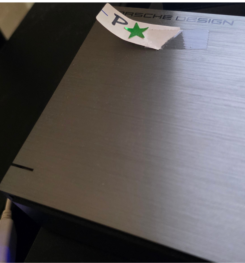 picture of an external PORSCHE DESIGN hard drive with a brushed-metal & black case and label taped-on with scotch tape with initial "P" and green foil star sticker